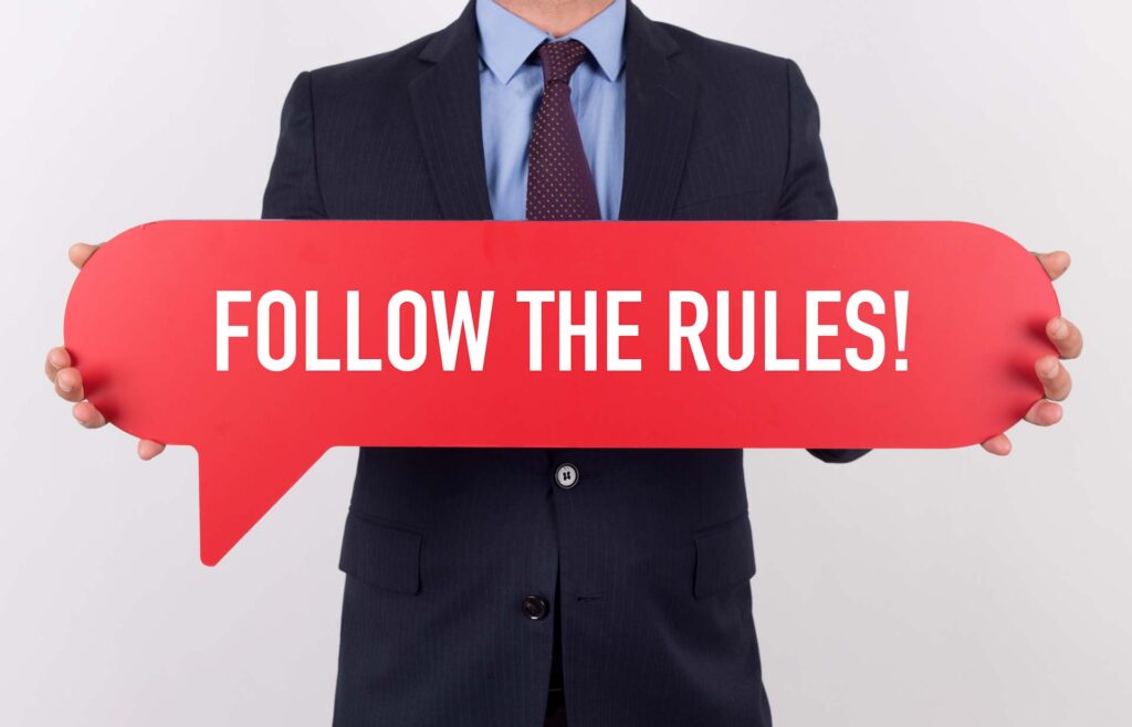 man holding a sign 'follow the rules'