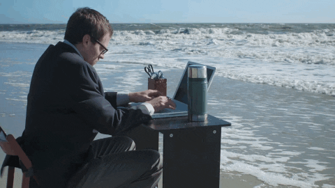 Funny work from home meme of a suited man at a beachside desk with waves crashing in, capturing work from home challenges, remote work memes, and virtual meetings gone wild.